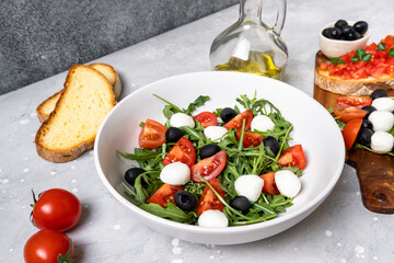 Lunch in Italian restaurant. mediterranean diet  food salad with arugula mozzarella tomatoes and olives, olive oil and fresh bread