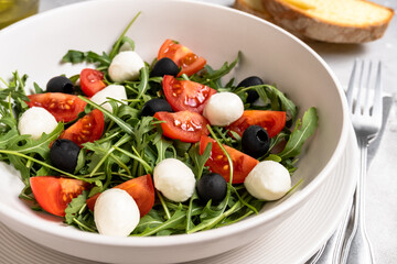 Lunch in Italian restaurant. mediterranean diet  food salad with arugula mozzarella tomatoes and olives, olive oil and fresh bread
