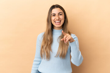 Young caucasian woman isolated on beige background surprised and pointing front