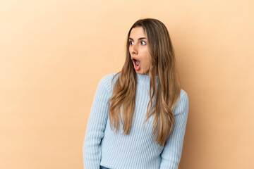 Young caucasian woman isolated on beige background doing surprise gesture while looking to the side