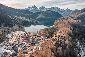 Aerial drone shot of Hohenschwangau by lake in Fussen with view of Alps snow mountain range in Germany winter