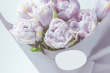 A bouquet of tulips wrapped in floral pale gray paper. White round shape label for logo insertion. Florist shop branding
