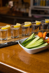tequila shot on bar table with lemon, salt, cucumber and carrot