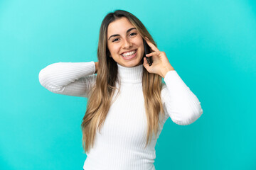 Young caucasian woman using mobile phone isolated on blue background laughing