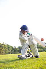 Obraz premium Young boy batting in protective gear during a cricket