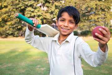 Portrait of a boy holding a cricket bat and a cricket ball