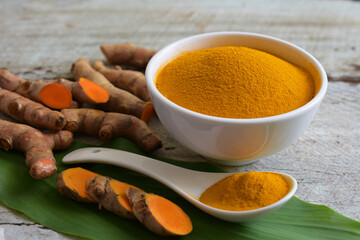 Turmeric (curcumin) powder in a white bowl and turmeric root on a wooden table,For cooking,Natural fabric dye,copy space.
