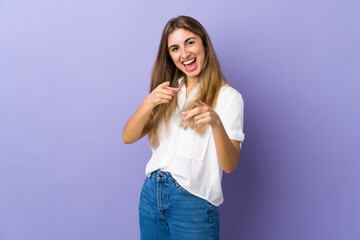 Young woman over isolated purple background surprised and pointing front