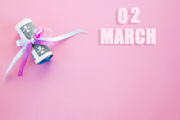 calendar date on pink background with rolled up dollar bills pinned by pink and blue ribbon with copy space. March 2 is the second day of the month