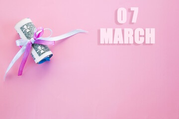 calendar date on pink background with rolled up dollar bills pinned by pink and blue ribbon with copy space. March 7 is the seventh day of the month