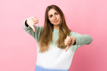 Young woman over isolated pink background showing thumb down with two hands