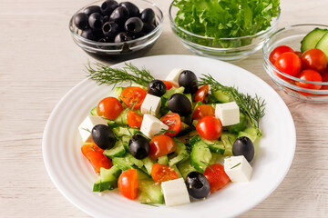Healthy vegetable salad with fresh products of cherry tomatoes, olives, fresh cucumber, feta with spices on a white plate. Healthy food concept. 