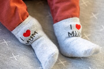 Obraz na płótnie Canvas A portrait of a baby's feet with gray socks and pants. On the cute socks the text, I love mum, is written. The child is lying on a grey pillow.