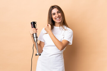 Woman using hand blender over isolated background celebrating a victory
