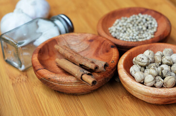 Fototapeta premium pepper, cardamom, and cinnamon in a wooden bowl on a wooden tray plus garlic and salt. close up with selective focus