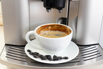 Brewing fresh coffee from your espresso machine. Budget coffee maker. White cup decorated with coffee beans.