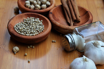 pepper, cardamom, and cinnamon in a wooden bowl on a wooden tray plus garlic and salt. close up with selective focus