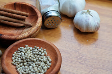 pepper, cardamom, and cinnamon in a wooden bowl on a wooden tray plus garlic and salt. close up with selective focus