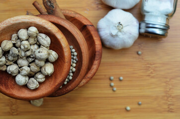 pepper, cardamom, and cinnamon in a wooden bowl on a wooden tray plus garlic and salt. close up with selective focus