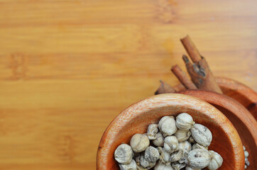 pepper, cardamom, and cinnamon in a wooden bowl on a wooden tray. close up with selective focus