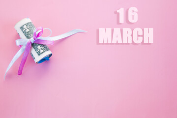 calendar date on pink background with rolled up dollar bills pinned by pink and blue ribbon with copy space. March 16 is the sixteenth day of the month