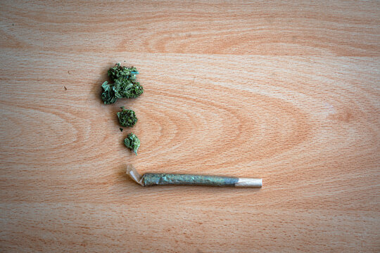 Rolled cannabis joint on a table with weed buds representing smoke