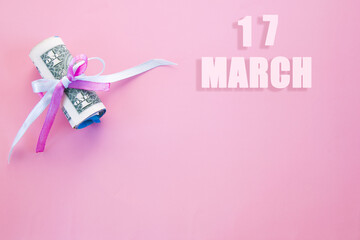 calendar date on pink background with rolled up dollar bills pinned by pink and blue ribbon with copy space. March 17 is the seventeenth day of the month