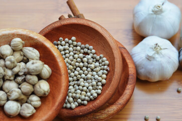 pepper, cardamom, and cinnamon in a wooden bowl on a wooden tray plus garlic and salt. close up with selective focus