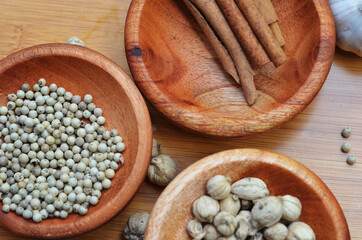 pepper, cardamom, and cinnamon in a wooden bowl on a wooden tray plus garlic and salt. close up with selective focus