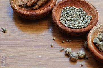 pepper, cardamom, and cinnamon in a wooden bowl on a wooden tray. close up with selective focus
