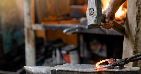 Blacksmith working metal detail with hammer on the anvil in rustic forge. Empty space for text