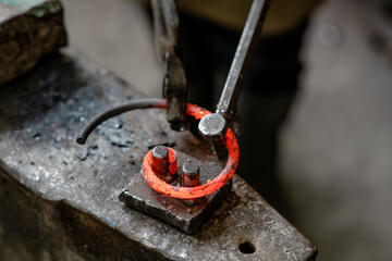 Close up blacksmith bends iron rod on the anvil with tool