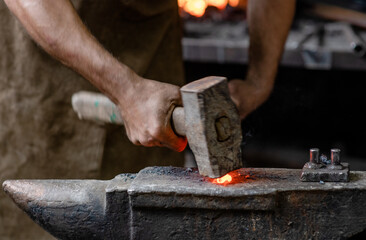 Close up blacksmith working metal with hammer on the anvil in the forge