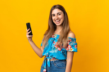 Young woman using mobile phone over isolated yellow background smiling a lot