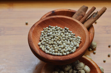 pepper, cardamom, and cinnamon in a wooden bowl on a wooden tray. close up with selective focus