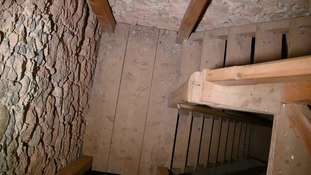 Wooden stairs in old castle tower. Underground staircase, mine entering concept. Old stone walls. Artificial light. Looking down, rotating