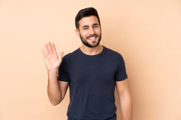 Fototapeta premium Caucasian handsome man isolated on beige background saluting with hand with happy expression