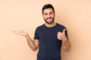 Caucasian handsome man isolated on beige background holding copyspace imaginary on the palm to...