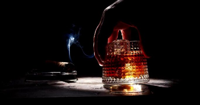 Glass of whiskey and smoking cigar on table. Slow motion, copy space, black background. Whiskey, brandy, cognac, alcoholic drink .