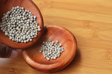 Asian man's hand poured the peppercorns into the wooden bowl. close up with selective focus