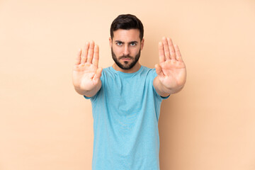 Caucasian handsome man isolated on beige background making stop gesture and disappointed