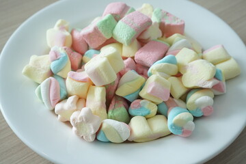 Colorful marshmallows on a white plate. Marshmallow is a type of confectionery that is typically made from sugar, water and gelatin whipped to a squishy consistency.