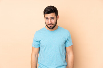 Caucasian handsome man isolated on beige background with sad expression