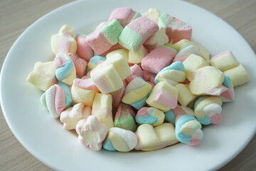 Colorful marshmallows on a white plate. Marshmallow is a type of confectionery that is typically made from sugar, water and gelatin whipped to a squishy consistency.
