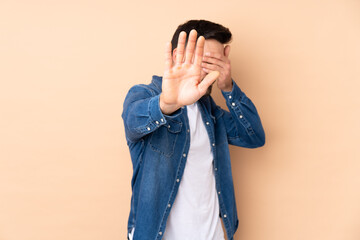 Caucasian handsome man isolated on beige background making stop gesture and covering face