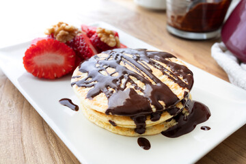 Homemade pancakes for breakfast and a good start to the day. Pancakes made with eggs, flour and yogurt. Pancakes with strawberries, hot chocolate and walnuts. Food photography