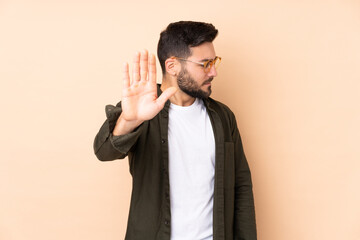 Caucasian handsome man isolated on beige background making stop gesture and disappointed