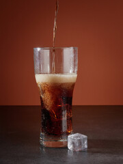 Soft drink glass with ice splash on dark background. Cola glass in celebration party concept.