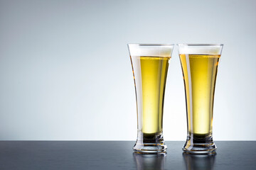 Two glass of beer on dark wooden table against grey background with copy space.