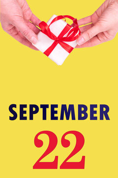 September 22nd. Festive Vertical Calendar With Hands Holding White Gift Box With Red Ribbon And Calendar Date 22 September On Illuminating Yellow Background. Autumn month, day of the year concept.